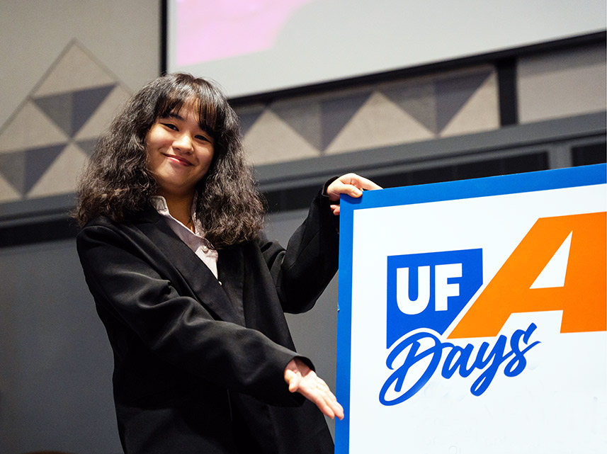 A UF student stands holding a large poster board that says AI Days