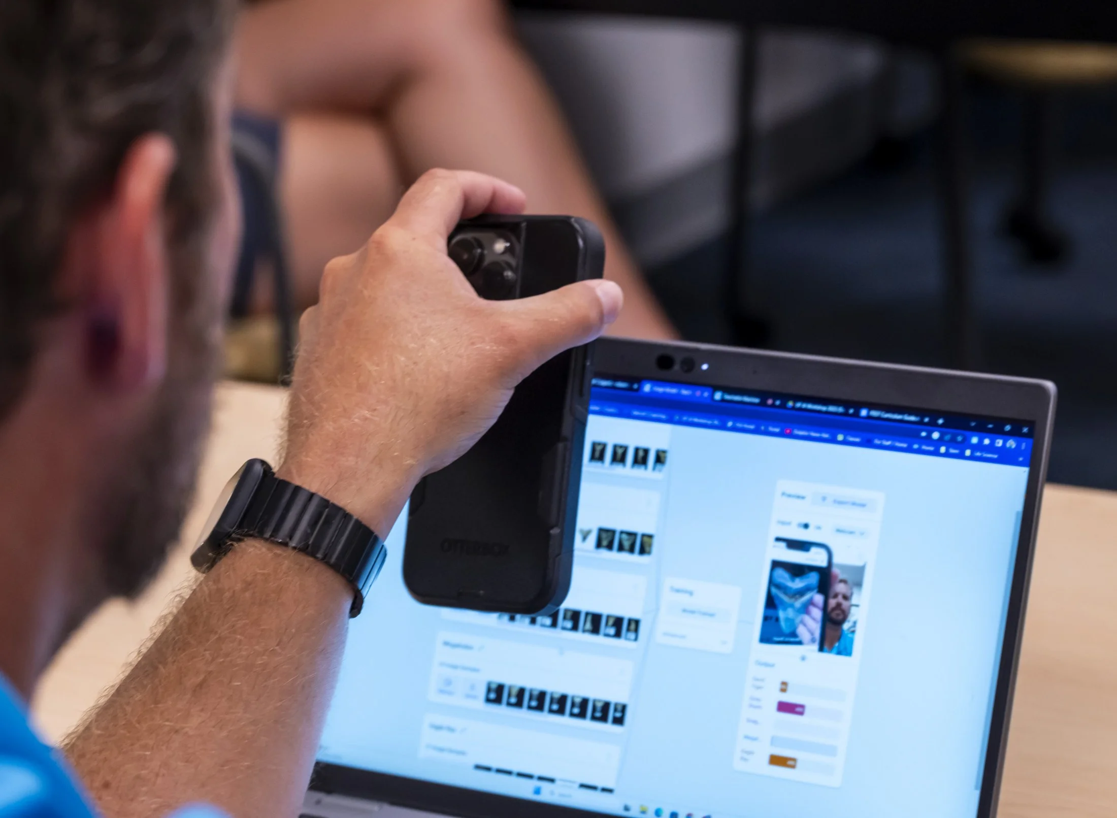 Man holding his phone in front of laptop camera