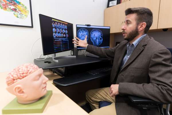 Photo of Dr. Joseph Gullett referring to a monitor that is depicting brain scans