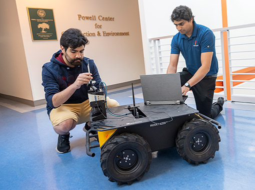 A student and a professor learn how to work a robot that is used in construction.